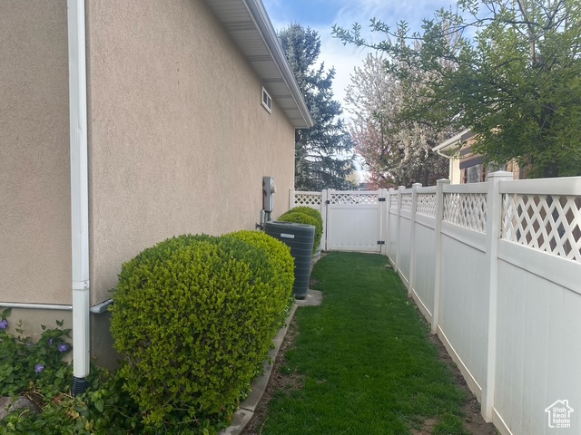 View of side of home with stucco siding, central AC, a fenced backyard, and a yard