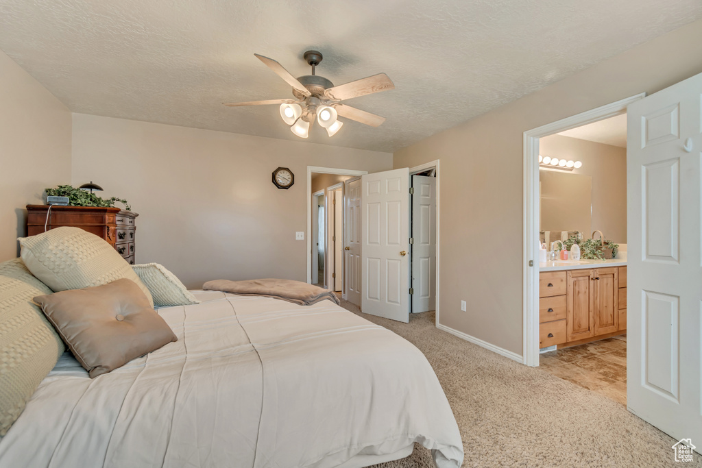 Bedroom featuring a textured ceiling, baseboards, connected bathroom, a ceiling fan, and light carpet