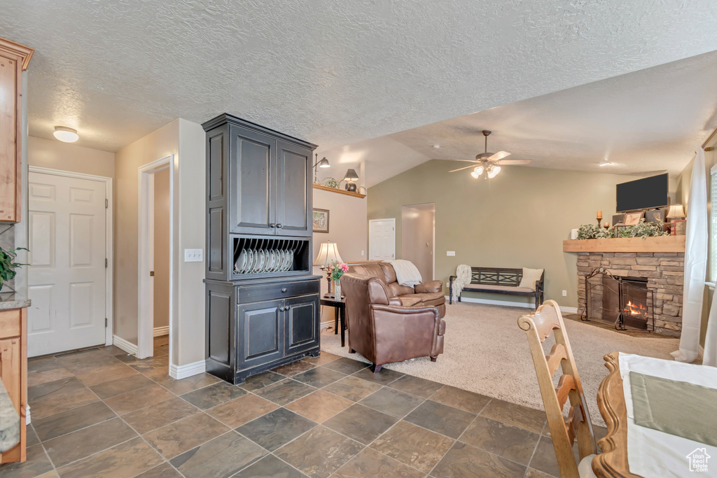 Living room featuring vaulted ceiling, a ceiling fan, a textured ceiling, a stone fireplace, and baseboards
