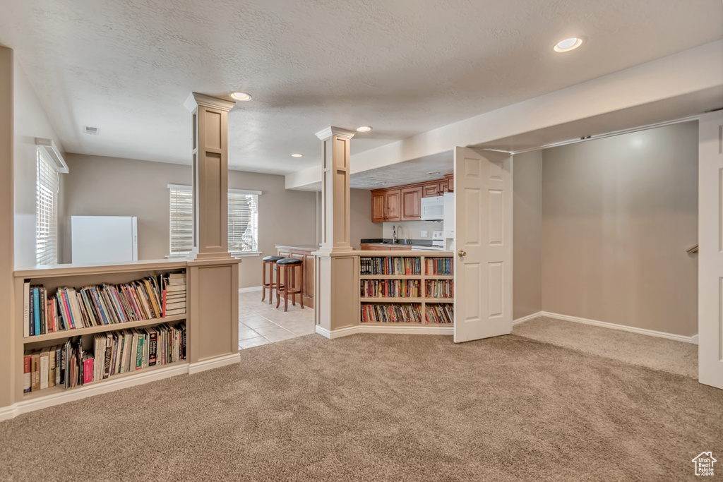 Interior space with decorative columns, baseboards, light colored carpet, and a textured ceiling
