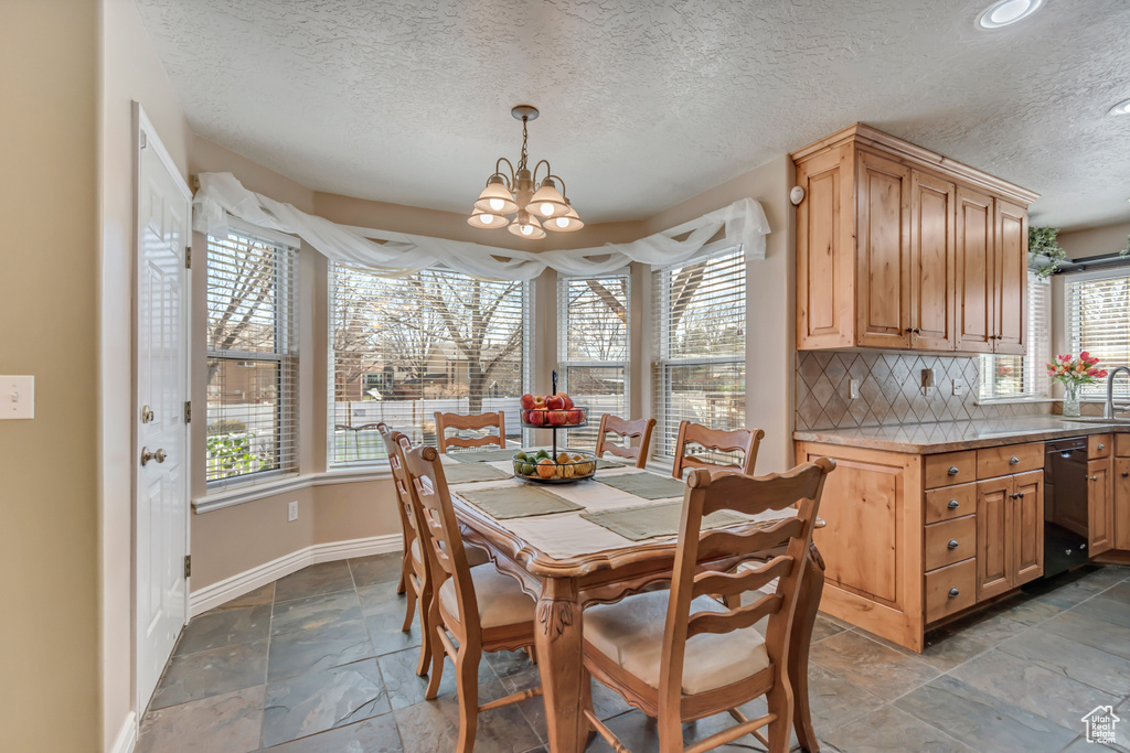 Dining space with an inviting chandelier, stone tile floors, baseboards, and a textured ceiling