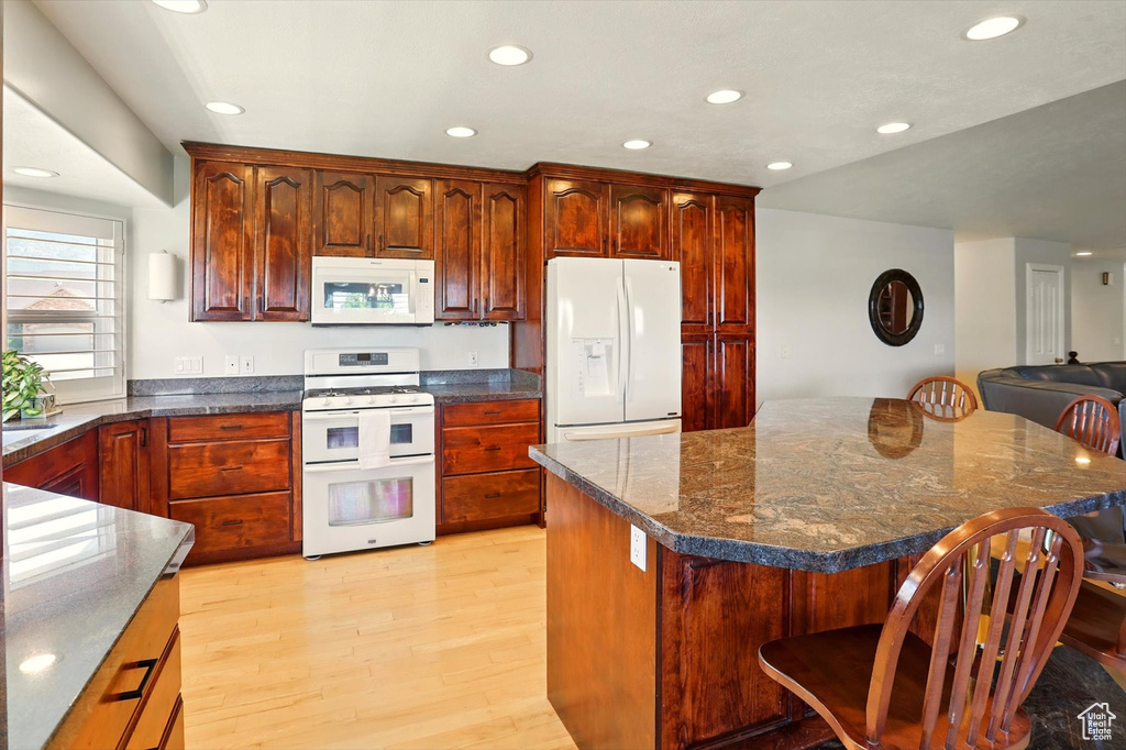 Kitchen with white appliances, light wood-style floors, recessed lighting, a breakfast bar, and dark stone counters