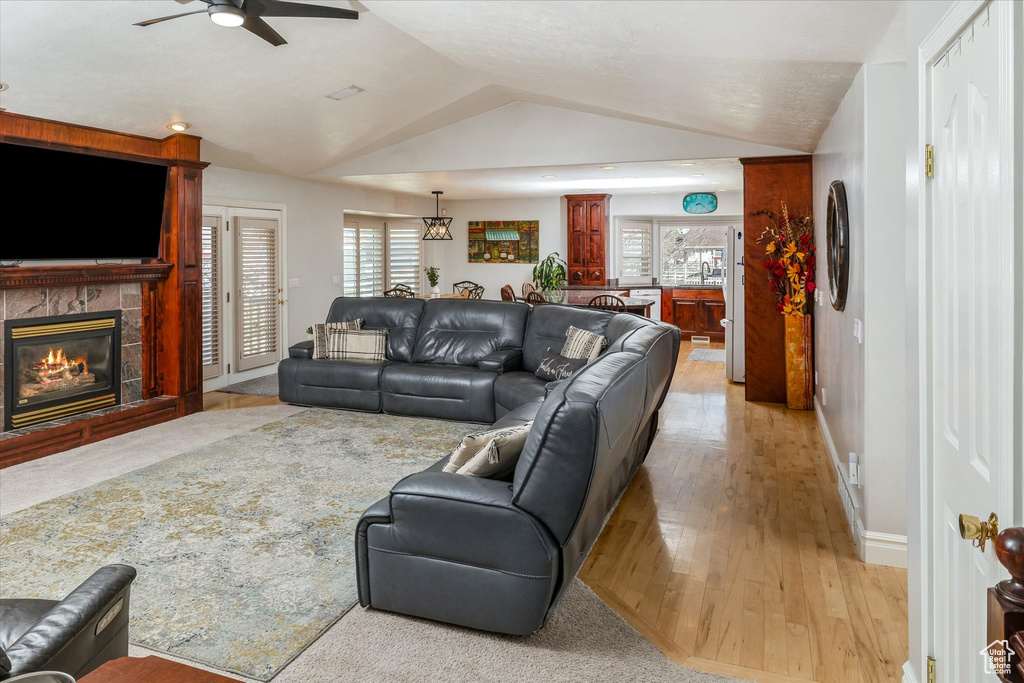 Living area featuring ceiling fan, light wood finished floors, lofted ceiling, and a tiled fireplace