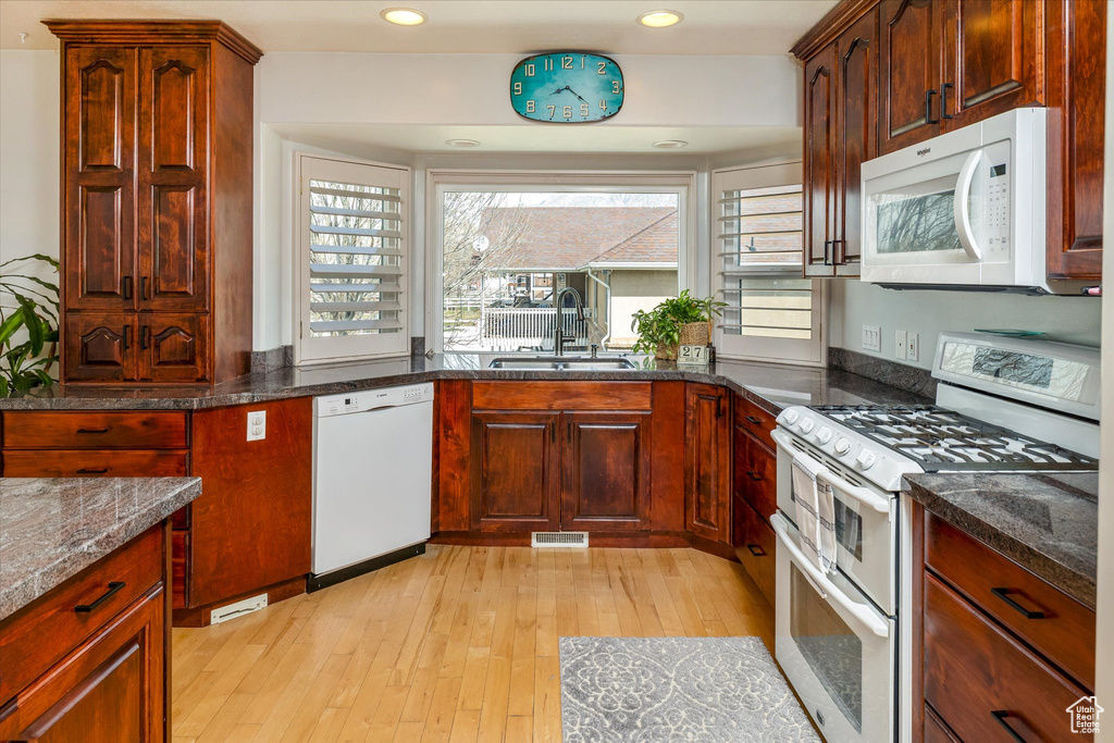 Kitchen featuring white appliances, light wood finished floors, dark stone countertops, and recessed lighting