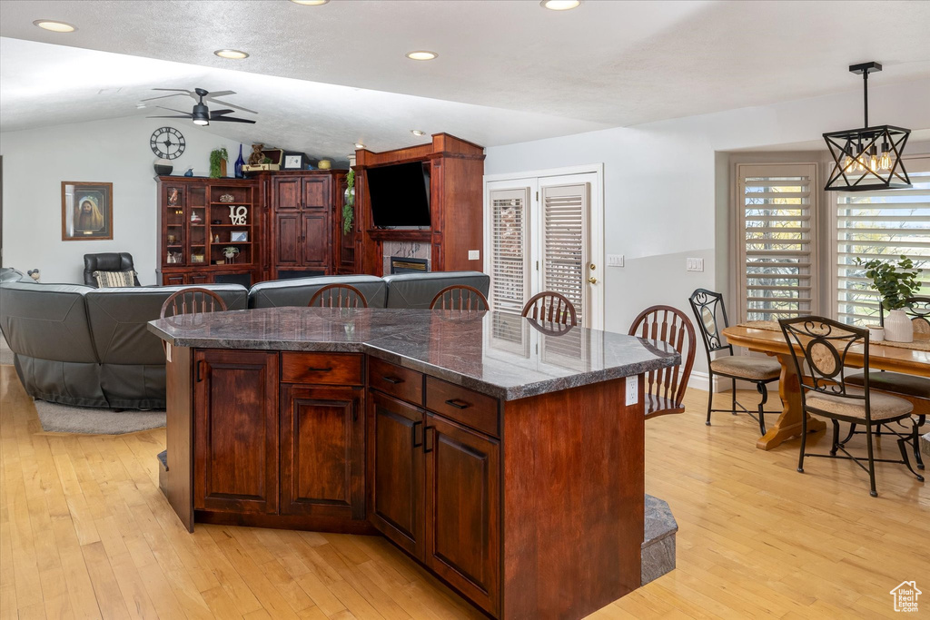 Kitchen featuring vaulted ceiling, a ceiling fan, light wood-style flooring, open floor plan, and a fireplace