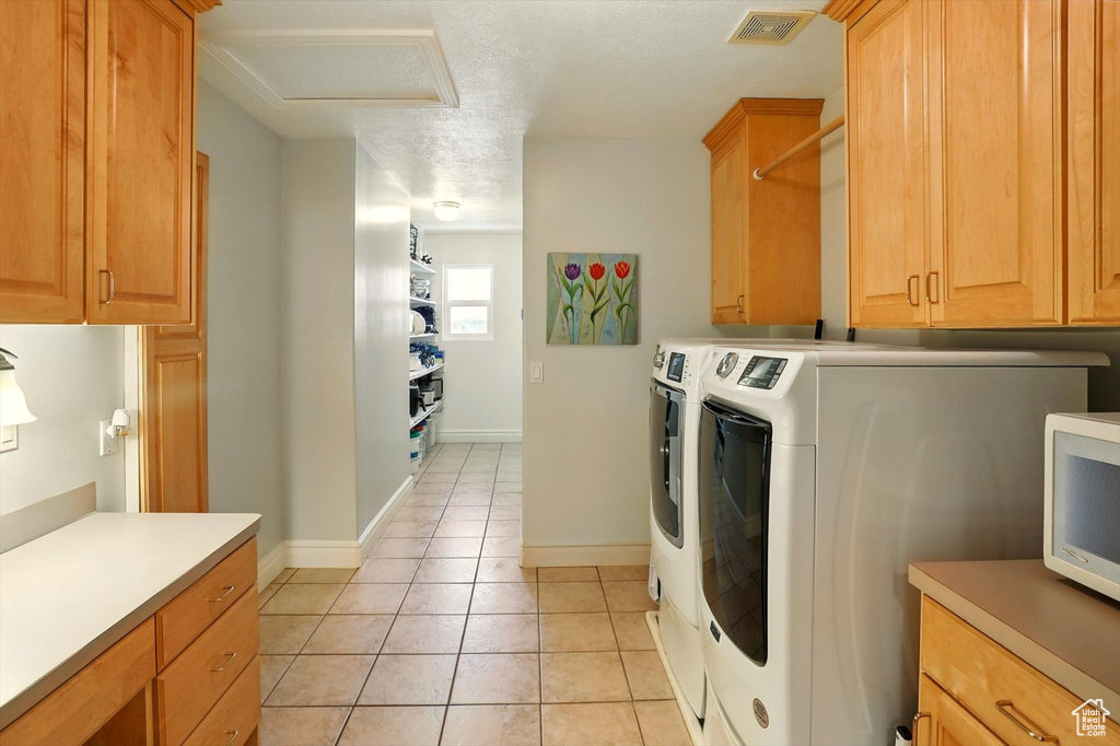 Laundry room featuring attic access, washer and dryer, light tile patterned flooring, and cabinet space