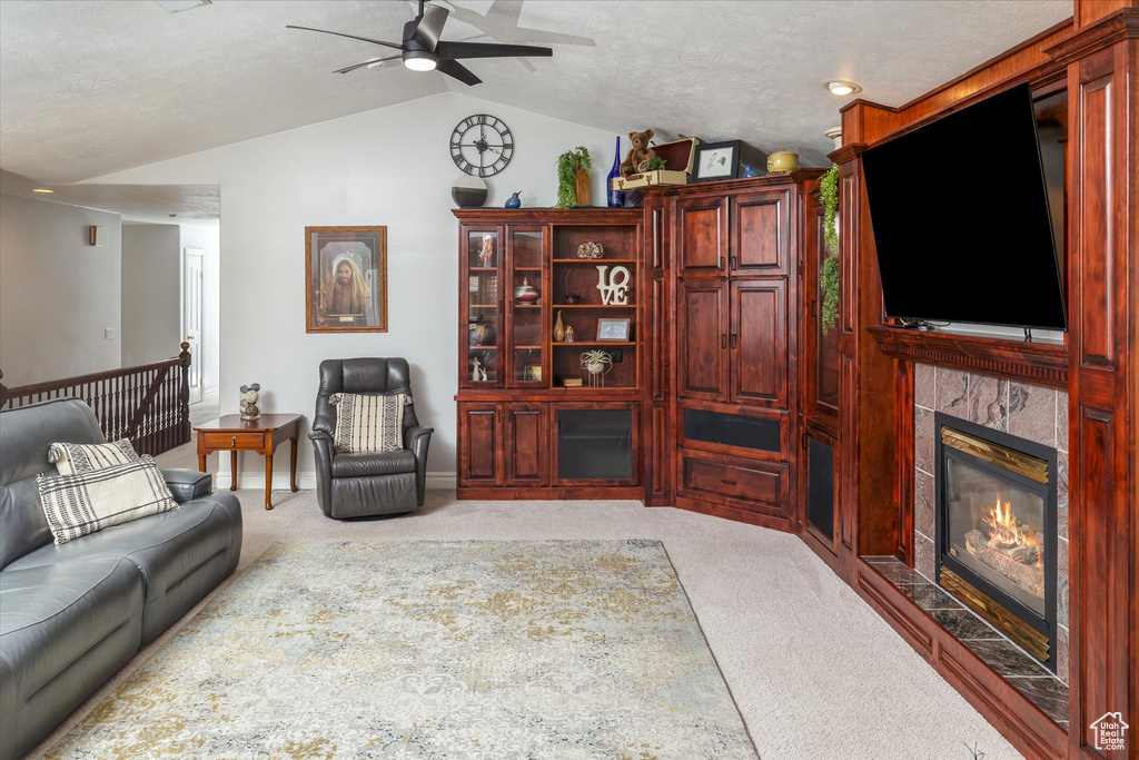 Carpeted living area with vaulted ceiling, ceiling fan, and a tile fireplace