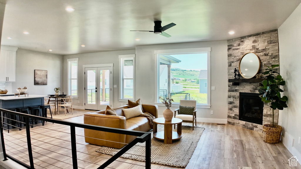 Living room with french doors, light wood-style flooring, a stone fireplace, a ceiling fan, and baseboards