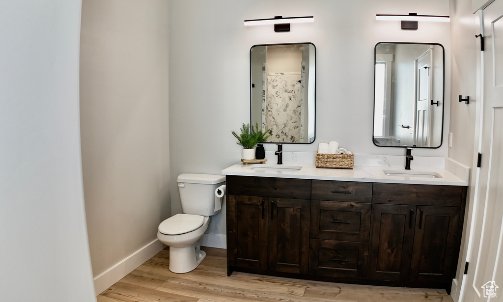 Full bath with toilet, double vanity, wood finished floors, and baseboards