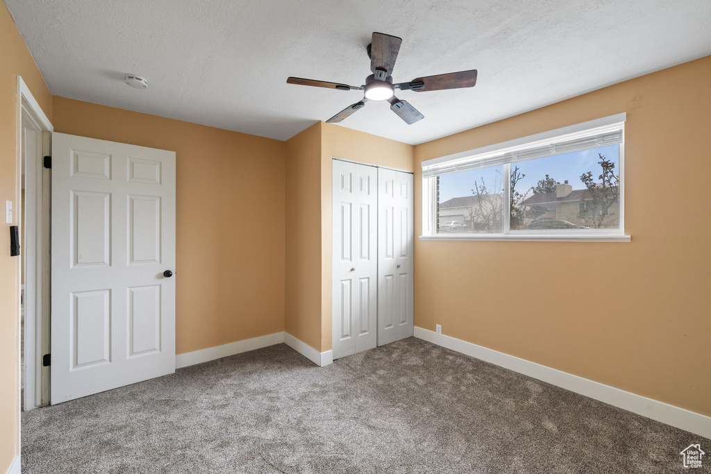 Unfurnished bedroom featuring a closet, a textured ceiling, carpet, baseboards, and ceiling fan