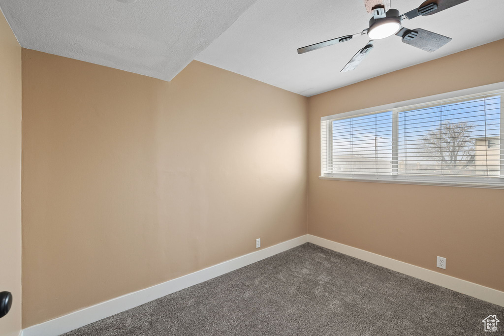 Empty room with baseboards, a ceiling fan, and dark colored carpet