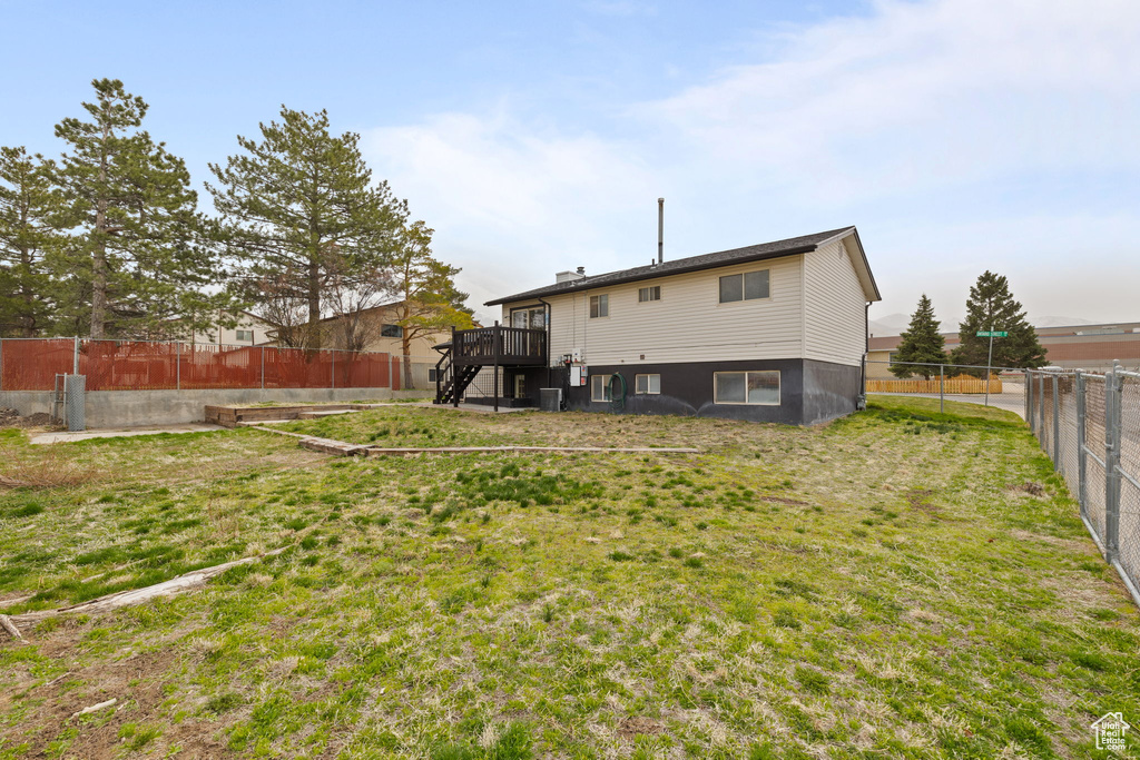 Rear view of house with stairway, central air condition unit, a deck, a fenced backyard, and a lawn