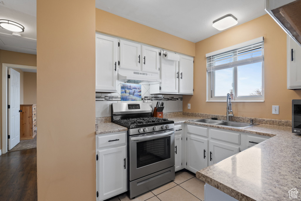 Kitchen with stainless steel range with gas stovetop, under cabinet range hood, backsplash, a sink, and white cabinets