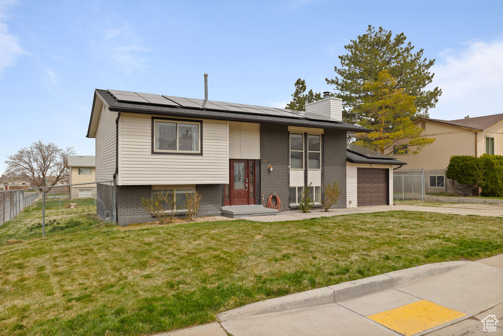 Bi-level home featuring an attached garage, a front lawn, roof mounted solar panels, and concrete driveway