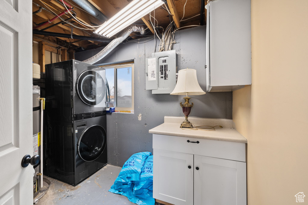 Laundry room featuring electric panel, cabinet space, and stacked washer / drying machine