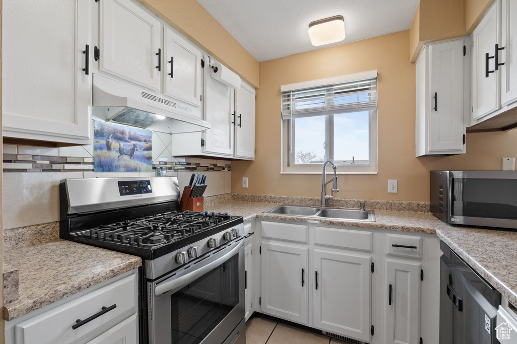Kitchen featuring light countertops, a sink, appliances with stainless steel finishes, under cabinet range hood, and white cabinets