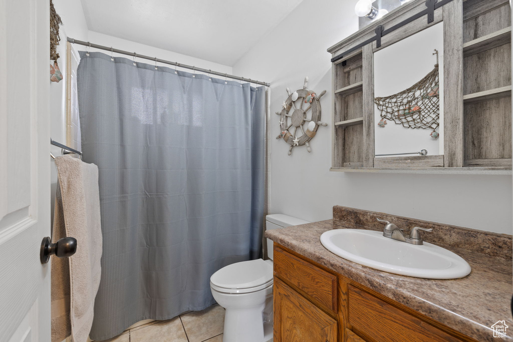 Bathroom with curtained shower, toilet, tile patterned floors, and vanity