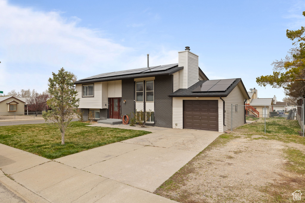 Bi-level home with fence, an attached garage, concrete driveway, brick siding, and a front lawn