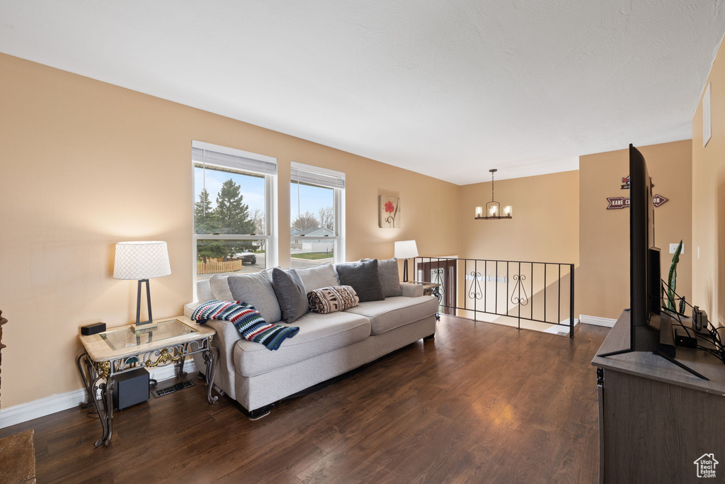 Living area with baseboards, a notable chandelier, and dark wood-style flooring