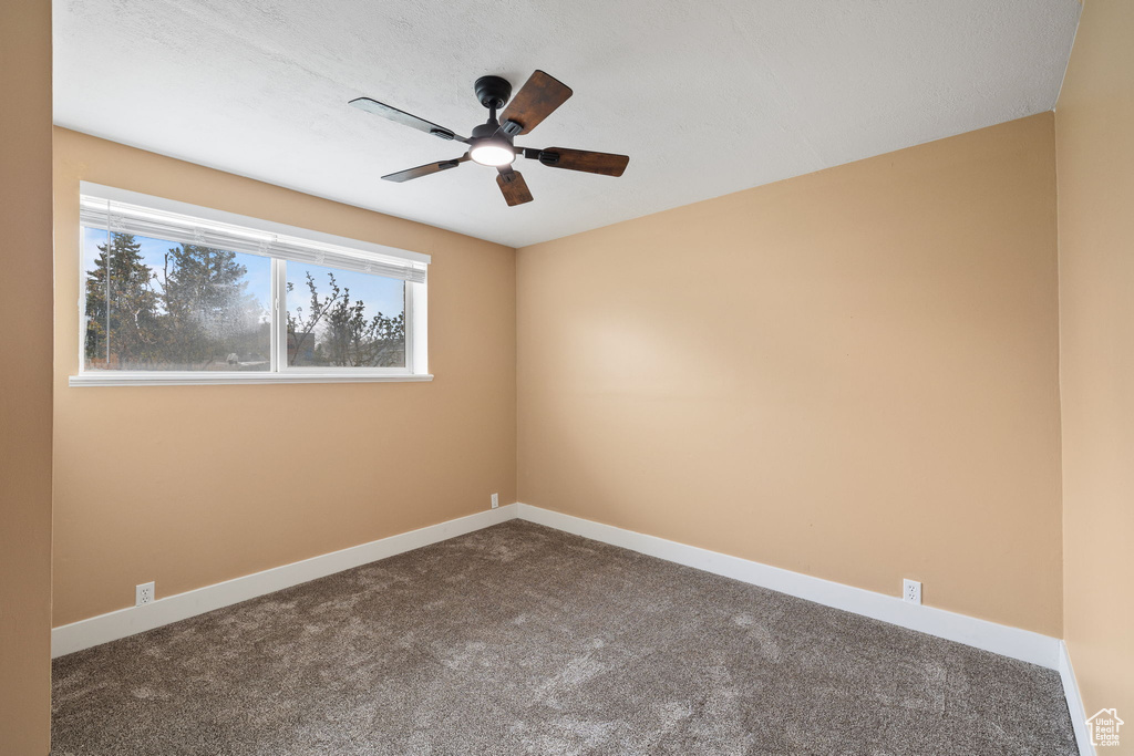 Unfurnished room with baseboards, dark colored carpet, and a ceiling fan