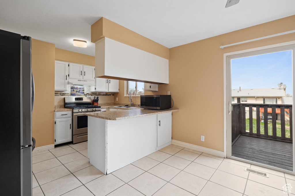 Kitchen featuring a peninsula, stainless steel appliances, under cabinet range hood, white cabinetry, and a sink