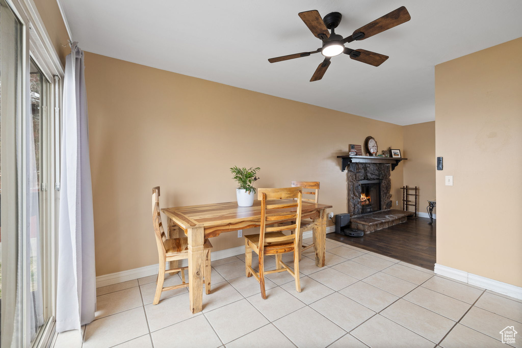 Dining space with light tile patterned flooring, baseboards, a fireplace, and a ceiling fan