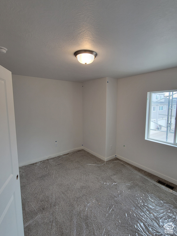 Carpeted empty room with baseboards, a textured ceiling, and visible vents