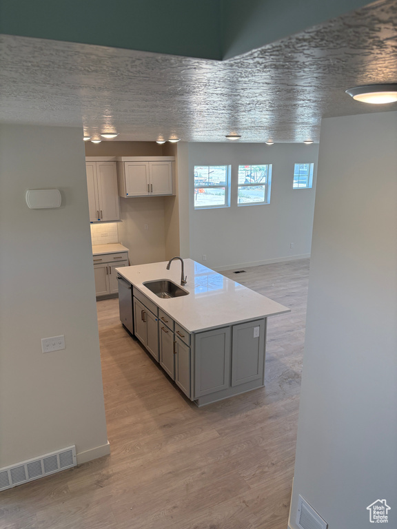 Kitchen with light wood-type flooring, light countertops, gray cabinets, a kitchen island with sink, and dishwasher