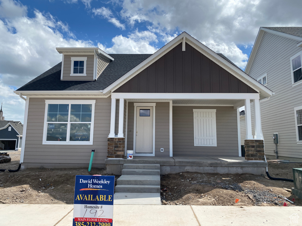 View of front of house featuring board and batten siding, roof with shingles, and covered porch