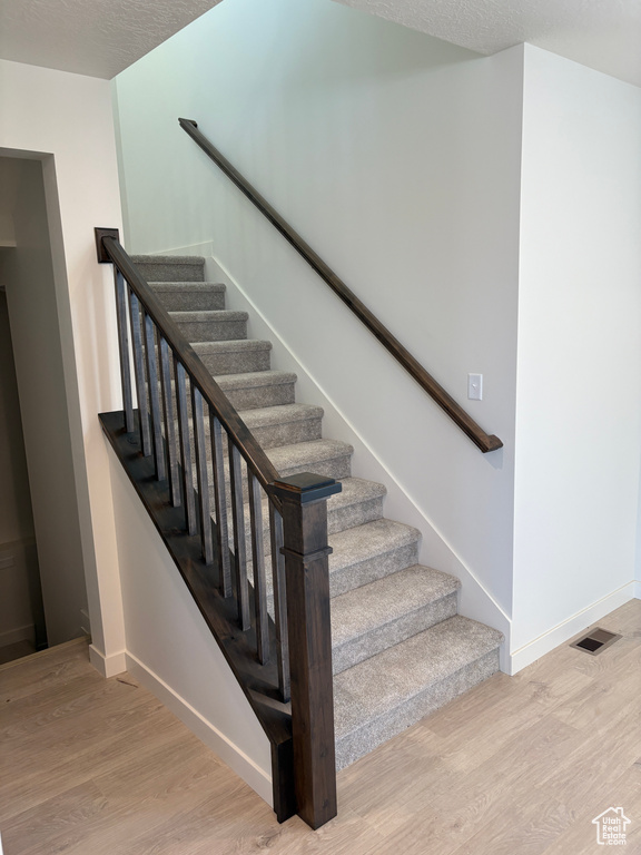 Stairway featuring wood finished floors and a textured ceiling