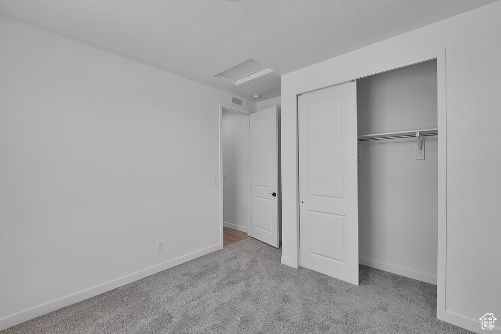 Unfurnished bedroom with carpet floors, attic access, baseboards, and a closet
