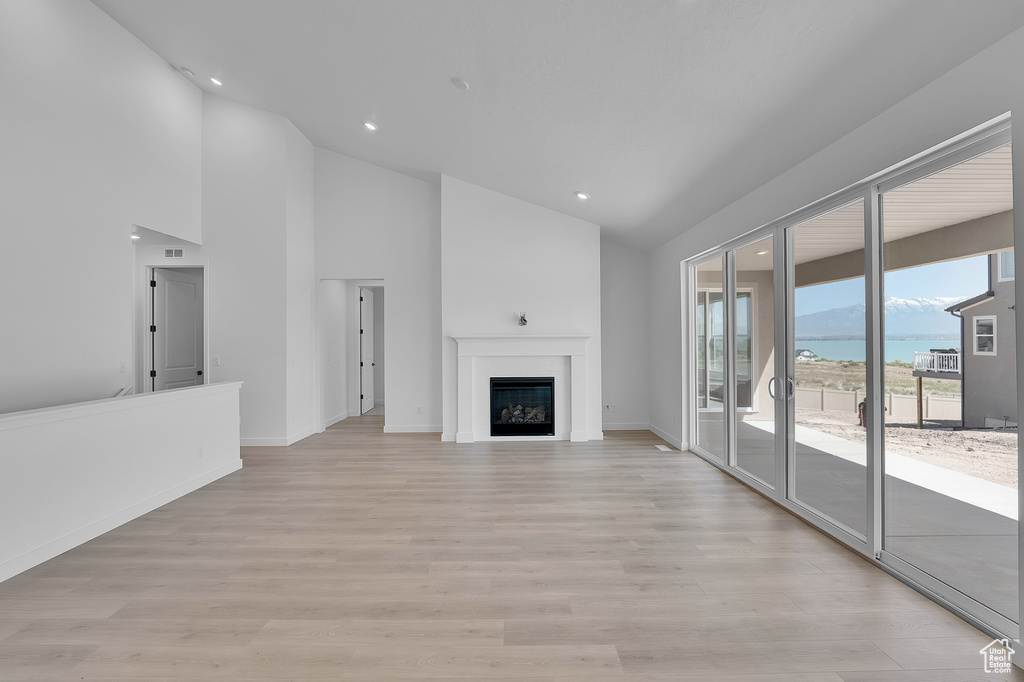 Unfurnished living room featuring a water view, light wood-type flooring, recessed lighting, a fireplace, and high vaulted ceiling