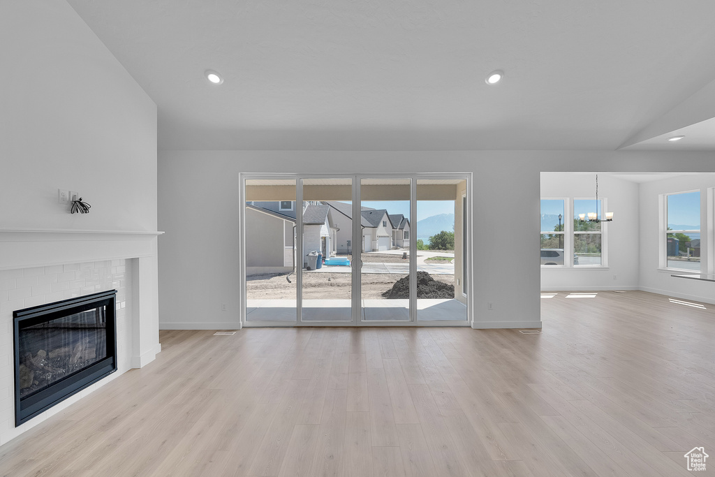 Unfurnished living room featuring a fireplace, light wood-style floors, baseboards, a chandelier, and recessed lighting