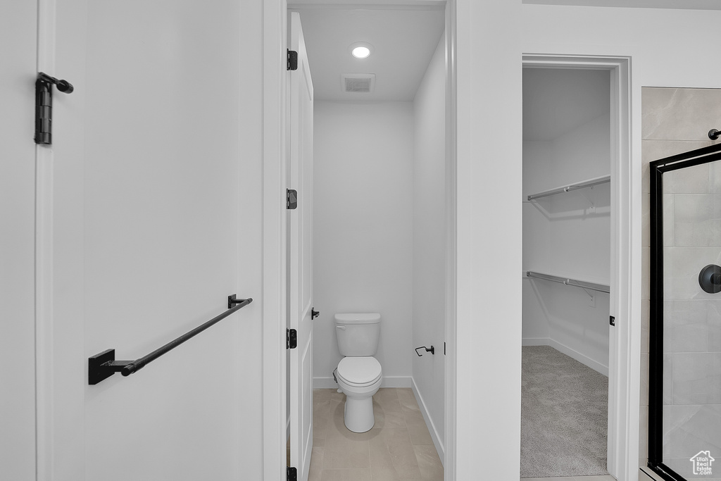 Bathroom featuring a shower stall, a spacious closet, toilet, and baseboards