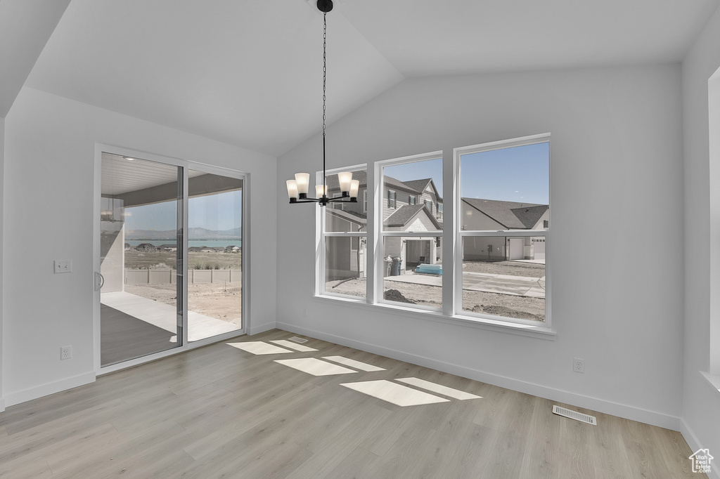Unfurnished dining area featuring healthy amount of natural light, a chandelier, vaulted ceiling, wood finished floors, and baseboards