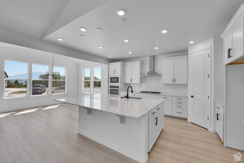 Kitchen featuring wall chimney exhaust hood, a sink, appliances with stainless steel finishes, light wood-style flooring, and recessed lighting