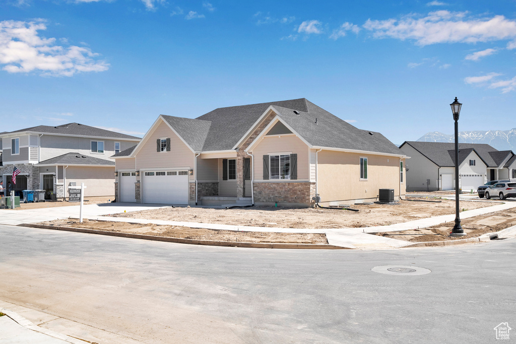 View of front facade with a garage, central AC unit, stone siding, a residential view, and driveway