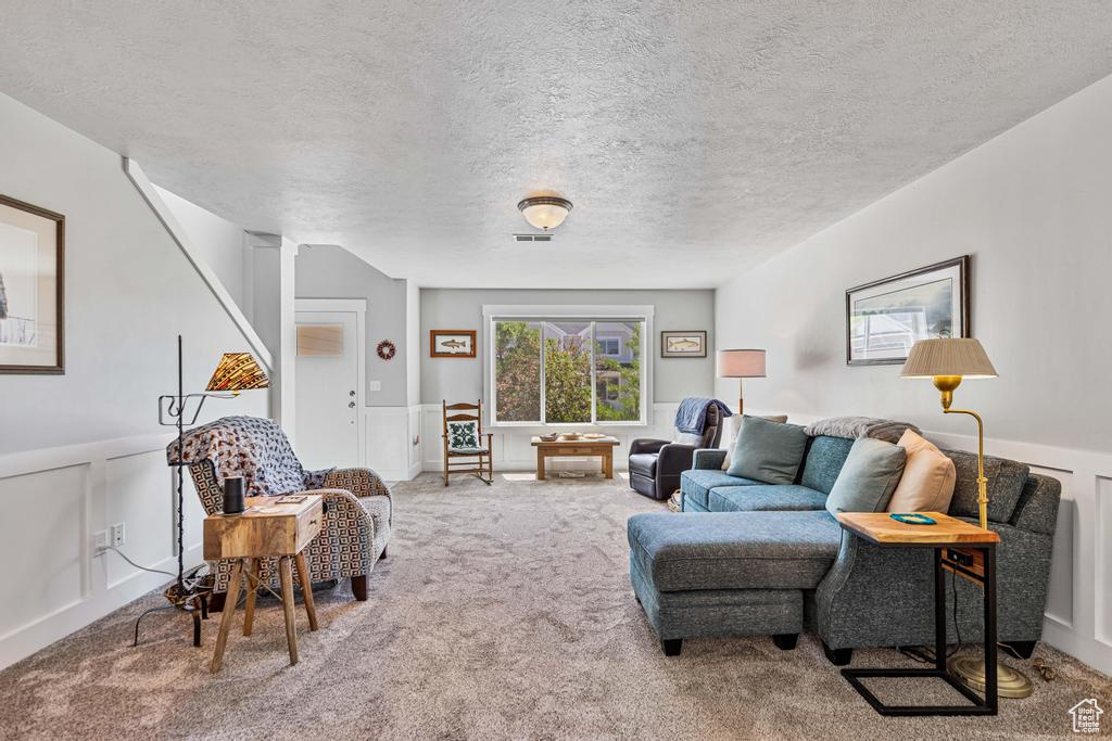 Carpeted living area featuring a textured ceiling, wainscoting, and a decorative wall
