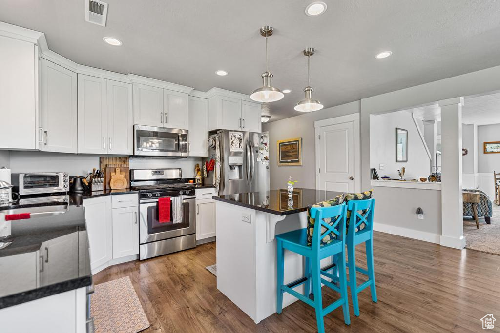 Kitchen featuring stainless steel appliances, white cabinets, a center island, dark wood-type flooring, and a kitchen breakfast bar