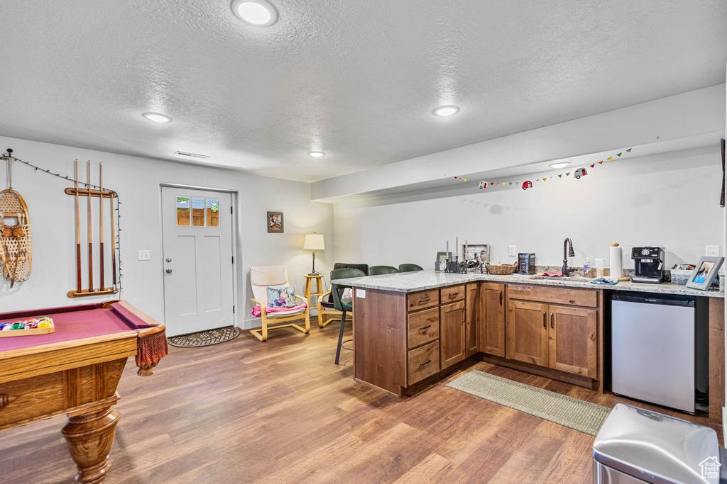 Kitchen featuring dishwasher, a peninsula, a sink, a textured ceiling, and brown cabinetry