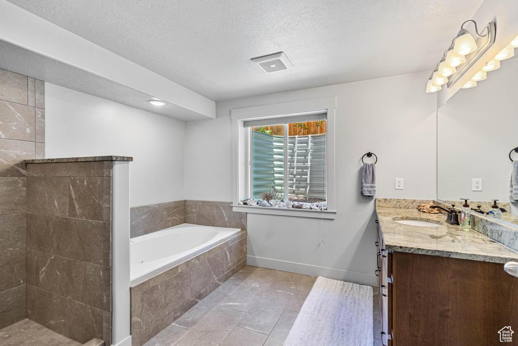 Full bathroom with vanity, a bath, a textured ceiling, baseboards, and tiled shower