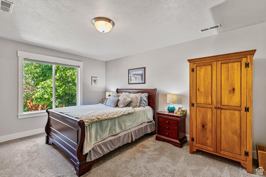 Bedroom with light colored carpet, a textured ceiling, and baseboards