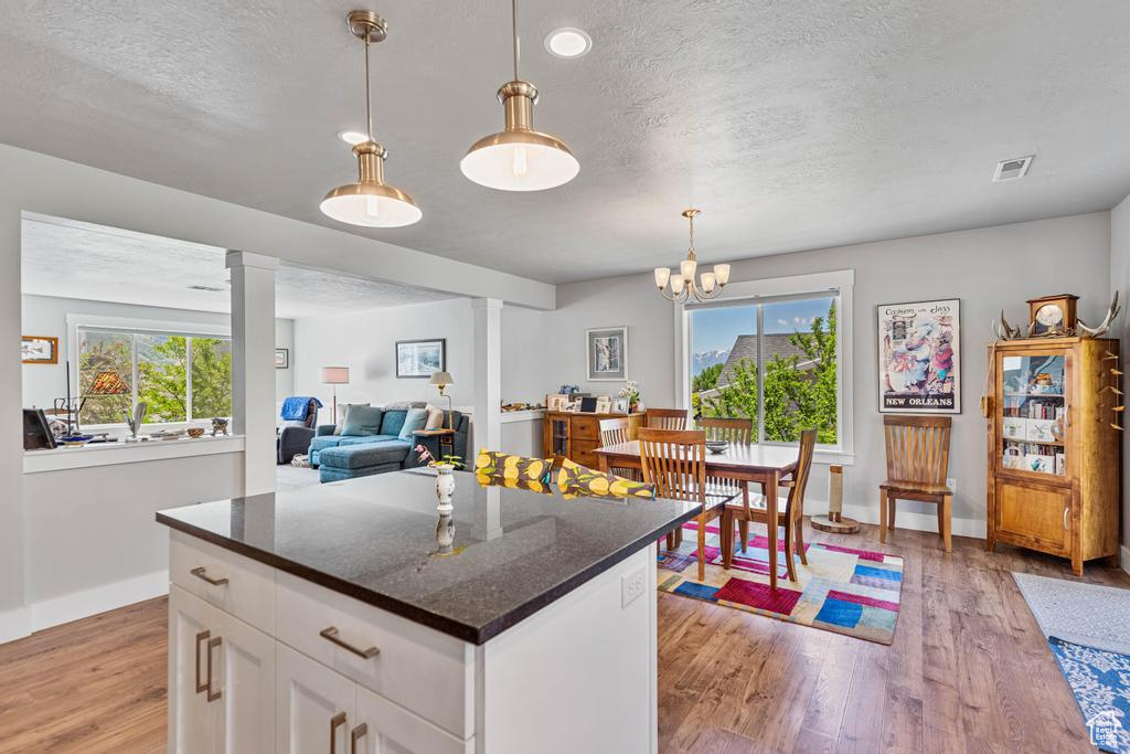 Kitchen with a textured ceiling, plenty of natural light, light wood-style floors, baseboards, and decorative columns