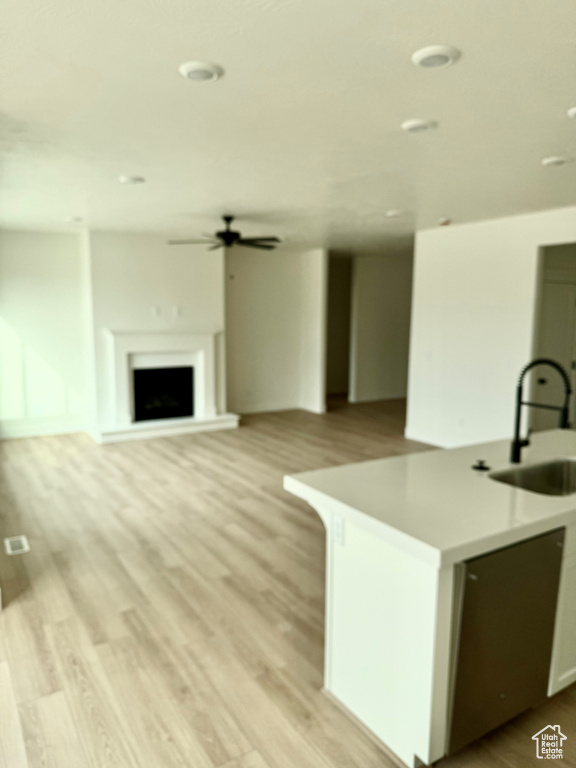 Kitchen featuring light countertops, a fireplace with raised hearth, a ceiling fan, a sink, and light wood-type flooring