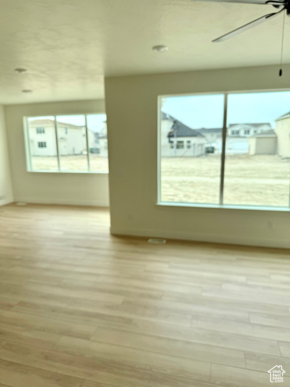 Unfurnished room featuring light wood finished floors, ceiling fan, and a healthy amount of sunlight