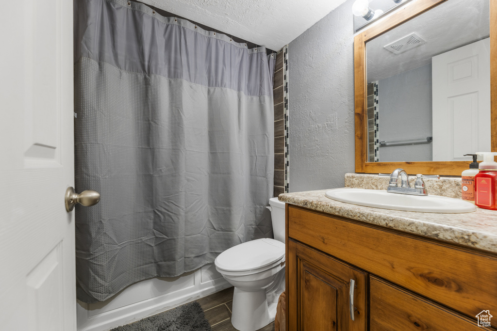 Full bath with vanity, a textured wall, shower / bath combo, toilet, and visible vents