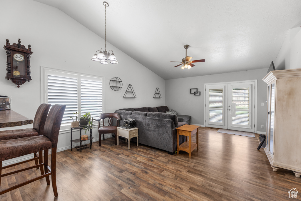 Living area featuring a wealth of natural light, dark wood-style flooring, ceiling fan with notable chandelier, and vaulted ceiling