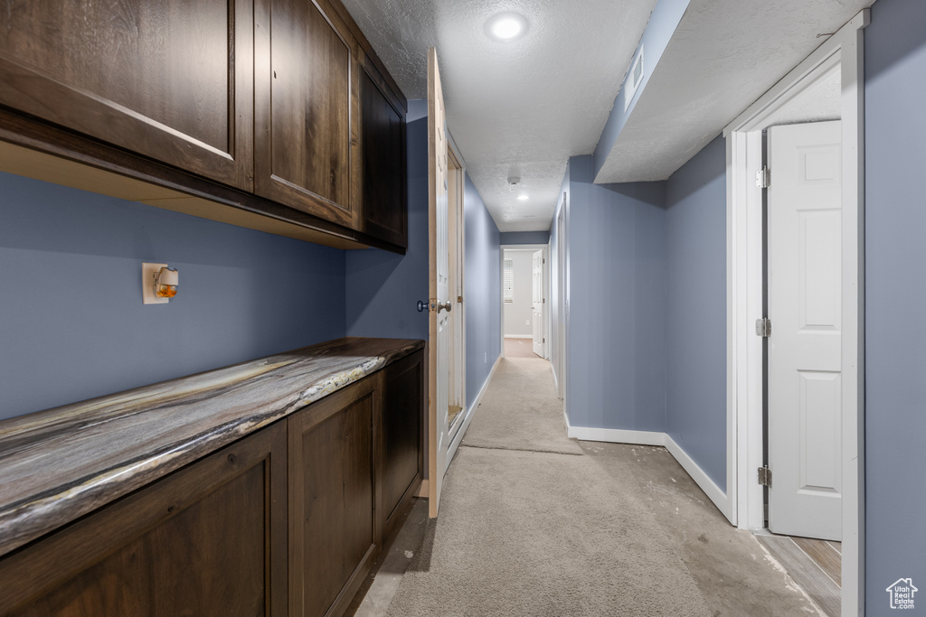 Hall with a textured ceiling, baseboards, and light carpet