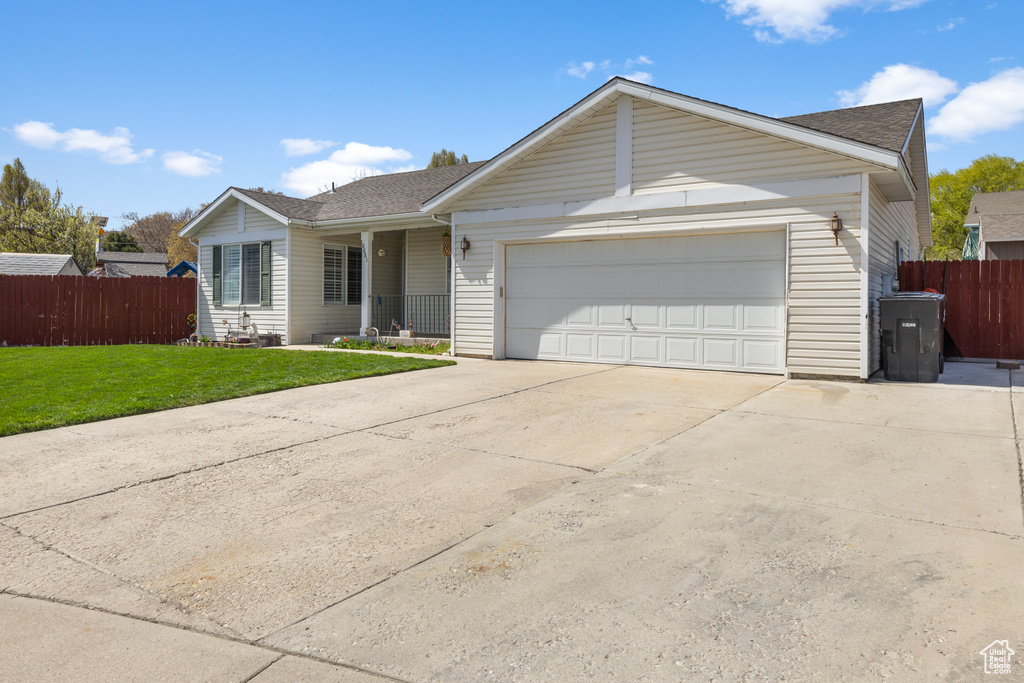 Ranch-style house with an attached garage, driveway, fence, and a front lawn
