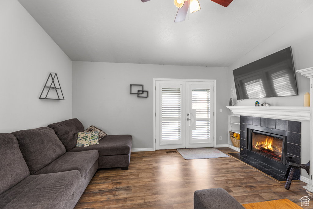 Living area featuring a ceiling fan, vaulted ceiling, wood finished floors, a tiled fireplace, and baseboards